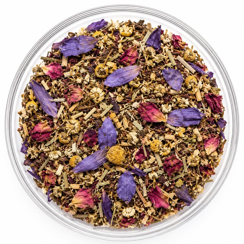 Wonder™ loose-leaf blend in a glass bowl — violet petals and magenta rose over pale chamomile heads and cut lemongrass