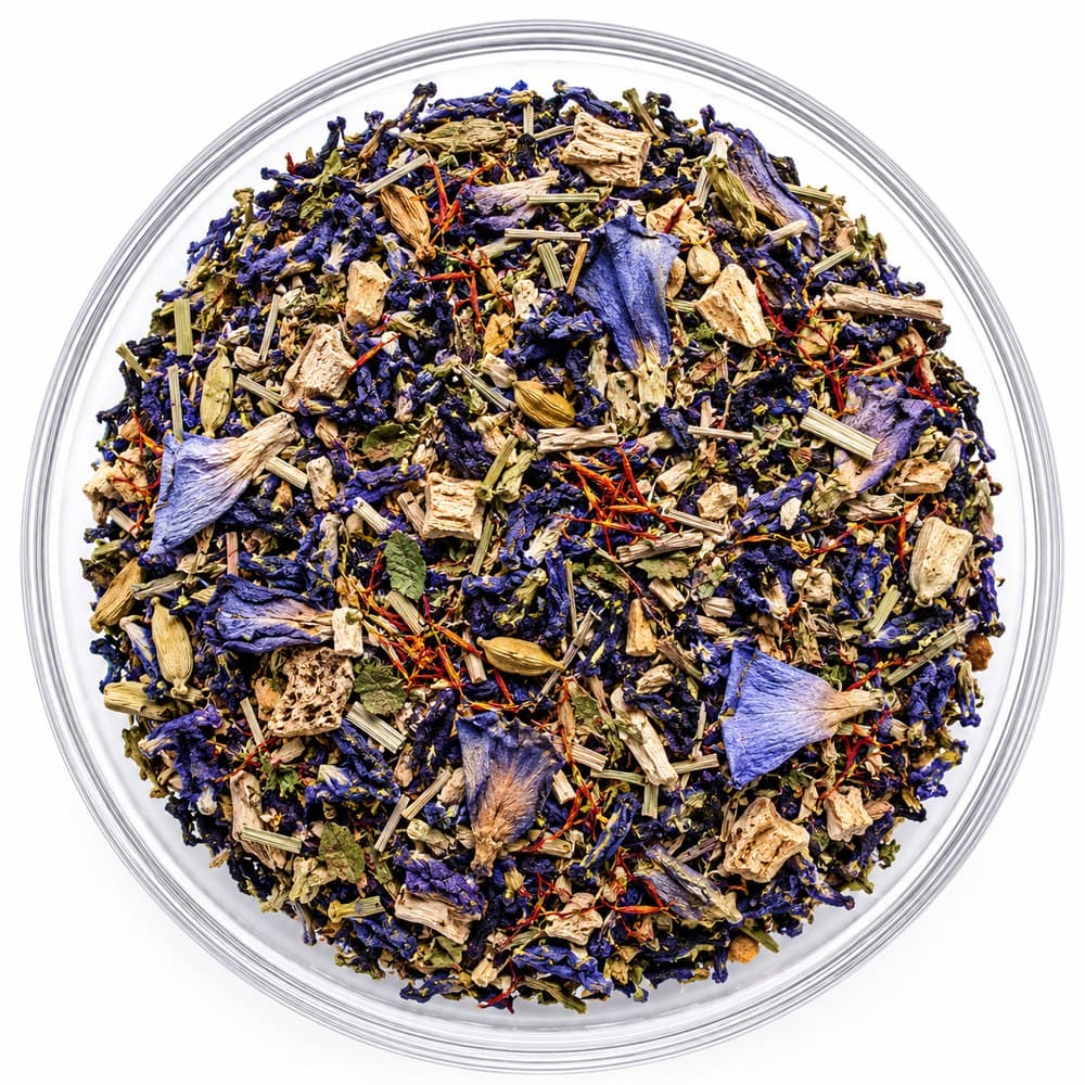 The Portal™ loose-leaf blend in a glass bowl — deep blue petals threaded with red-orange, green cardamom pods and cut lemongrass